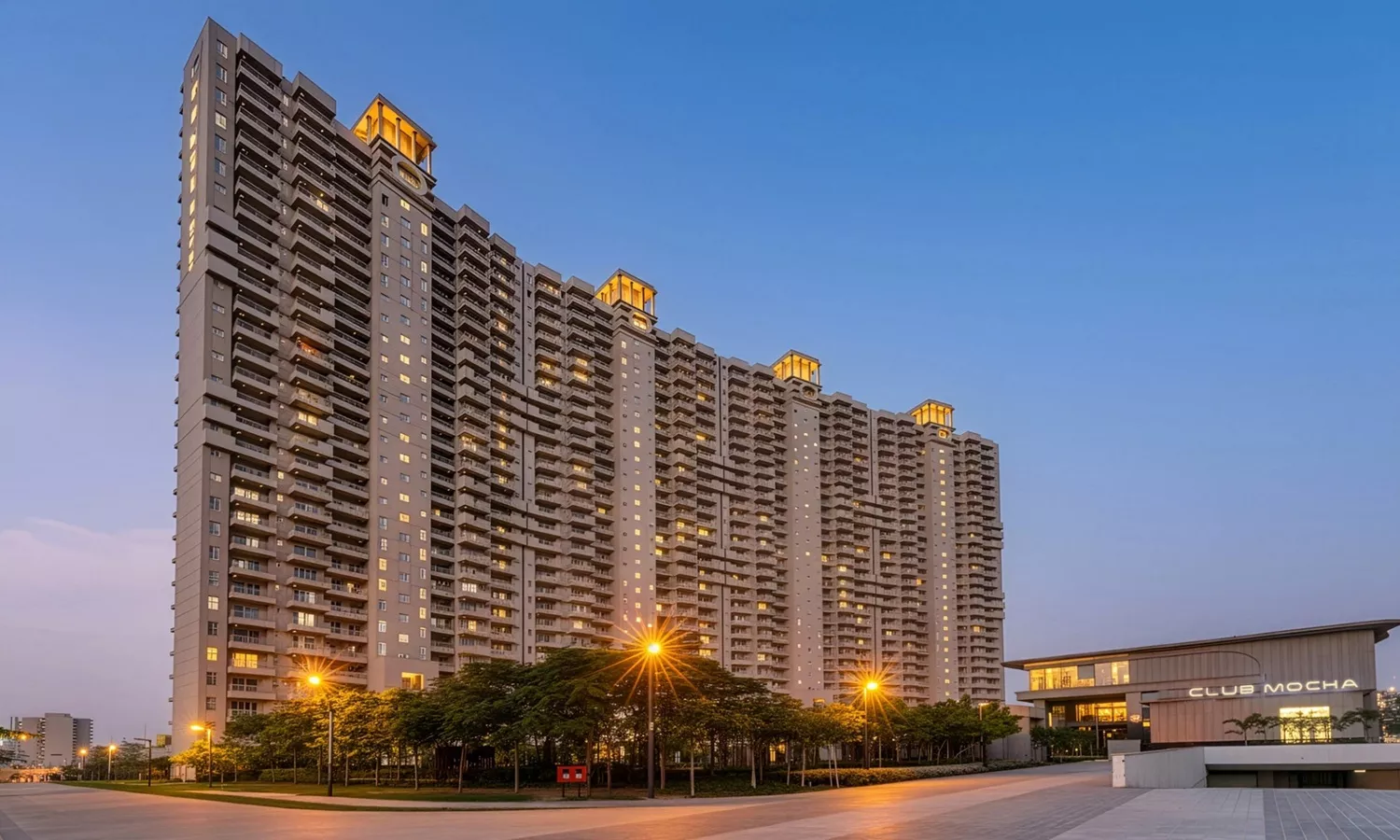 Evening view of  County residential towers in Sector 88A Gurgaon with Club Mocha clubhouse, illuminated tower facades and landscaped driveway in the foreground